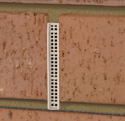 A long, narrow white metal or plastic Weepa vent grille with multiple rectangular slots, shown vertically against a textured terracotta brick wall. To stop insects, rodents and sparks.